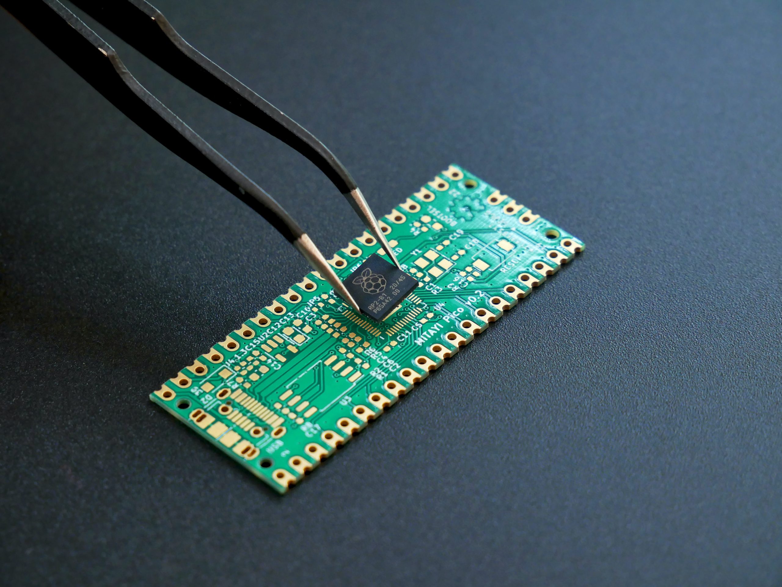 Un microcontrôleur RP2040 tenu avec une pincette au-dessus d'un PCB.